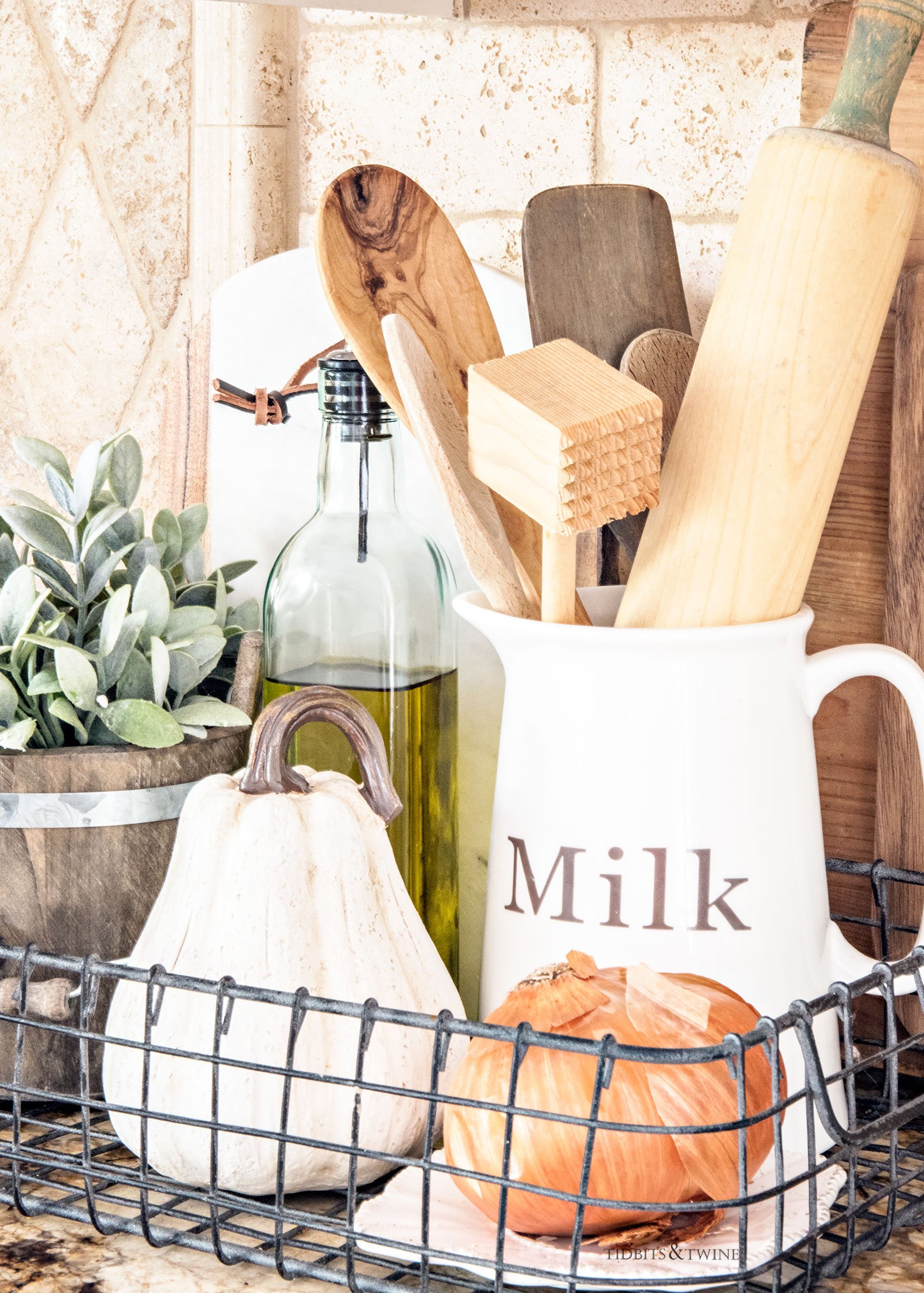 Fall kitchen vignette of wire basket holding wooden utensils a bottle of olive oil and a small white pumpkin