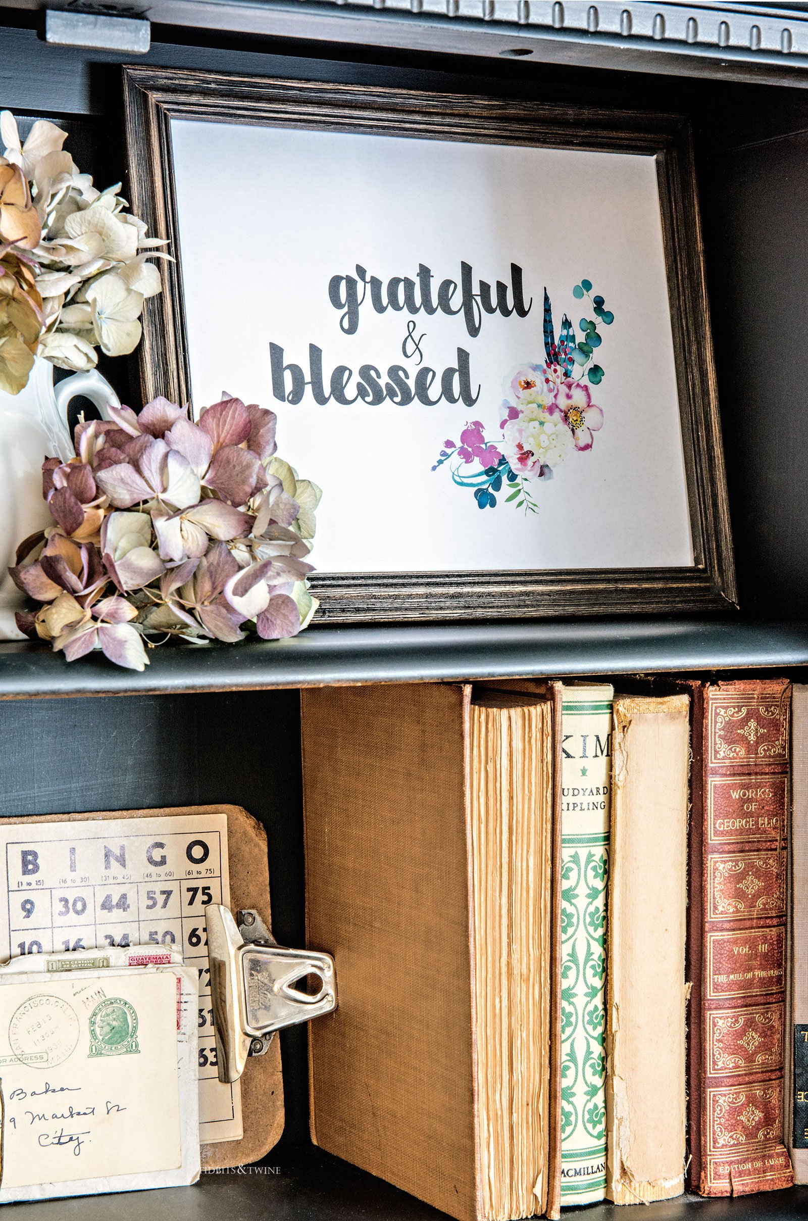 Free fall printable in a black cabinet with dried hydrangea next to the frame and antique books on the shelf below