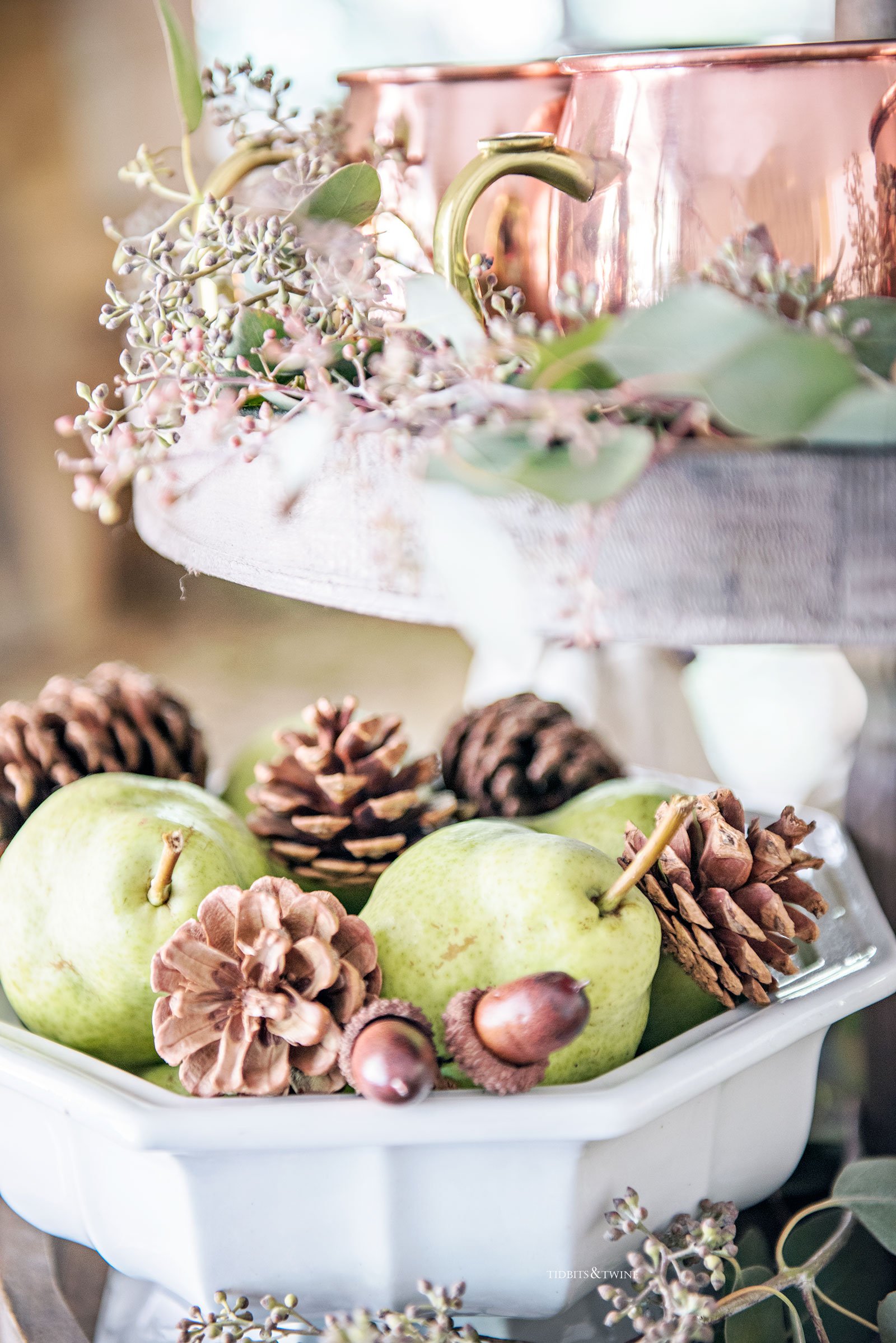 tiered kitchen tray with white ironstone bowl fulls of pears and pinecones with copper mugs and eucalyptus on tier above 