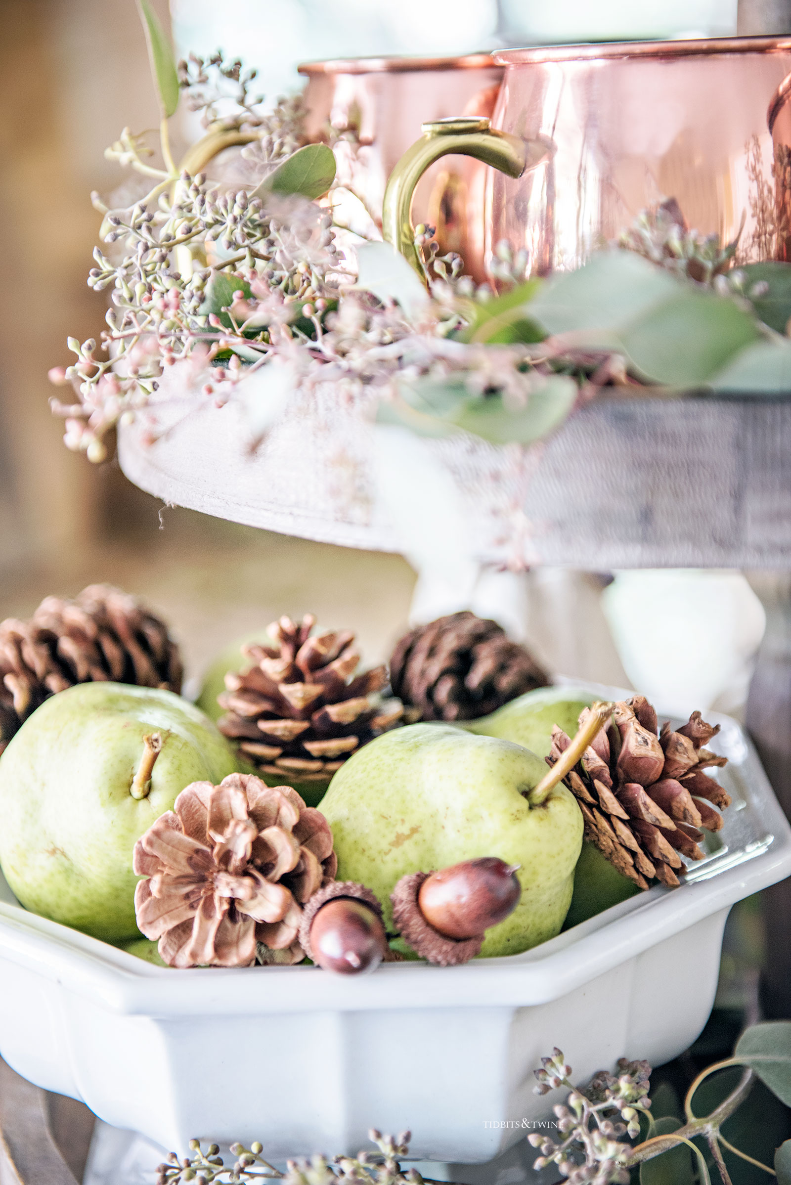tiered kitchen tray with white ironstone bowl fulls of pears and pinecones with copper mugs and eucalyptus on tier above