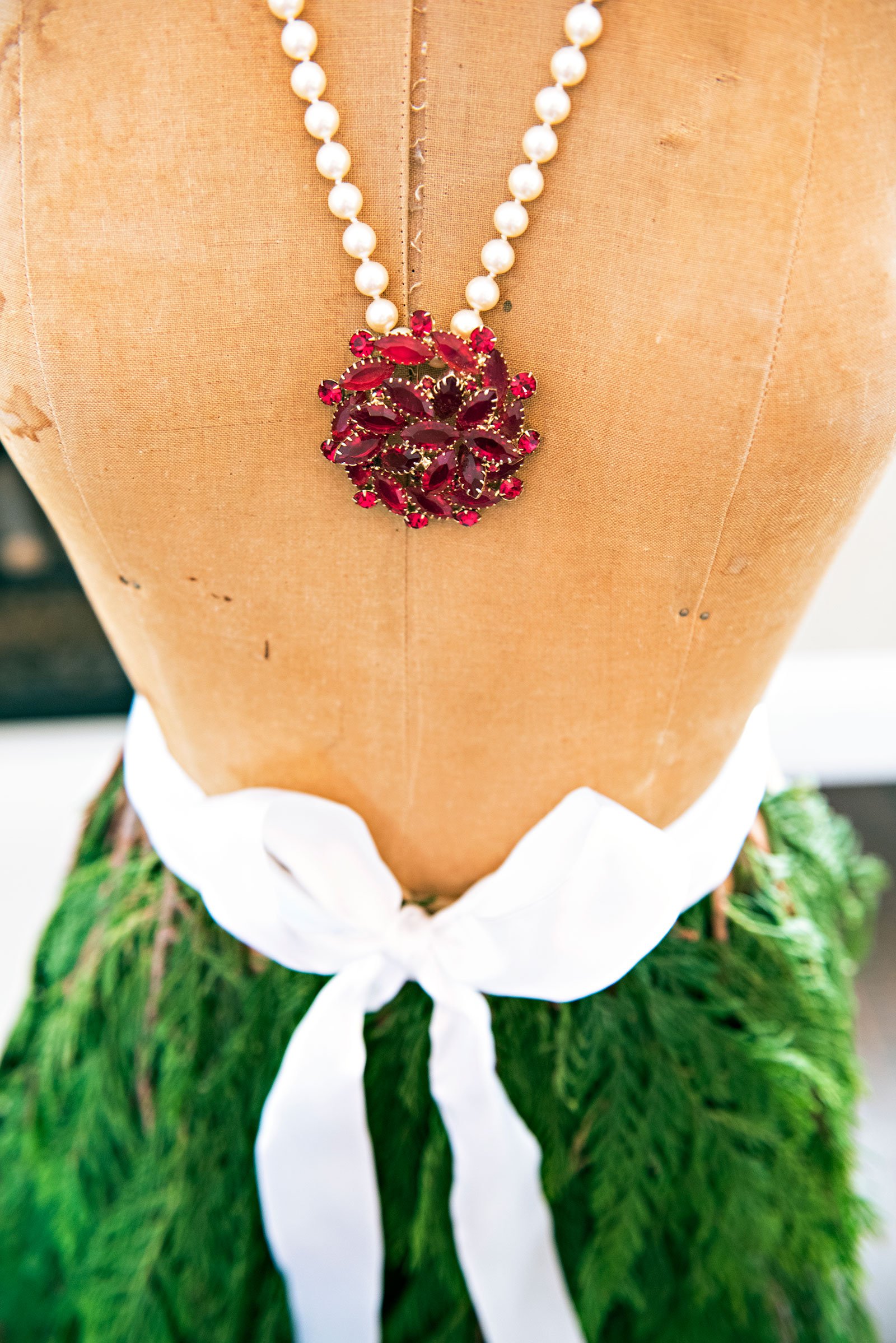 Vintage dress form with red broach and pearl necklace and cedar skirt tied with a white bow