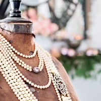 brown antique dress form with multiple strands of white pearls around neck and pink and green christmas decor in background