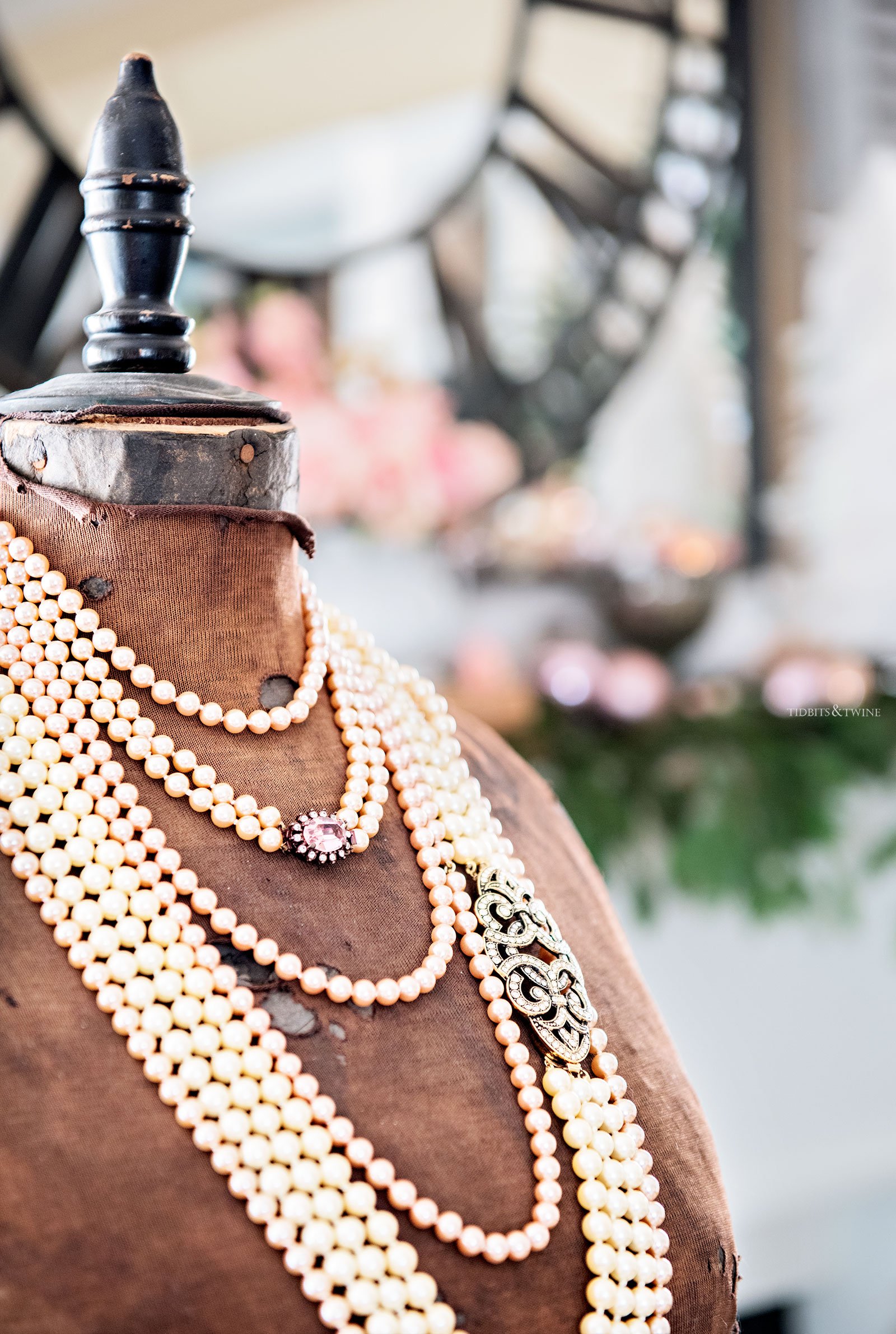 brown antique dress form with multiple strands of white pearls around neck and pink and green christmas decor in background