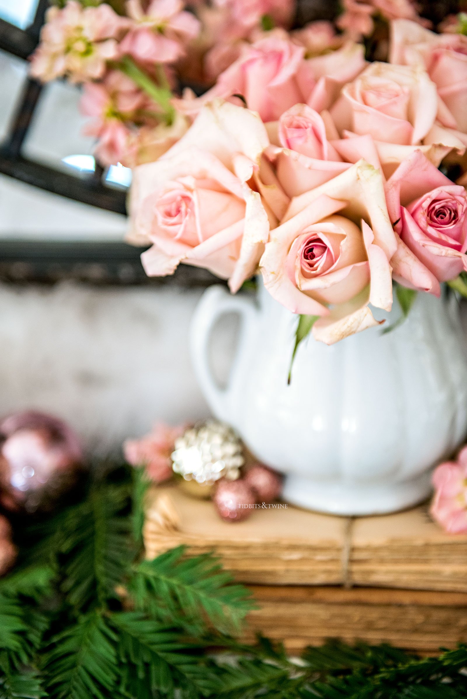 light pink roses in white ironstone sugar bowl on top of antique books with cedar branches and small pink christmas ornaments at base