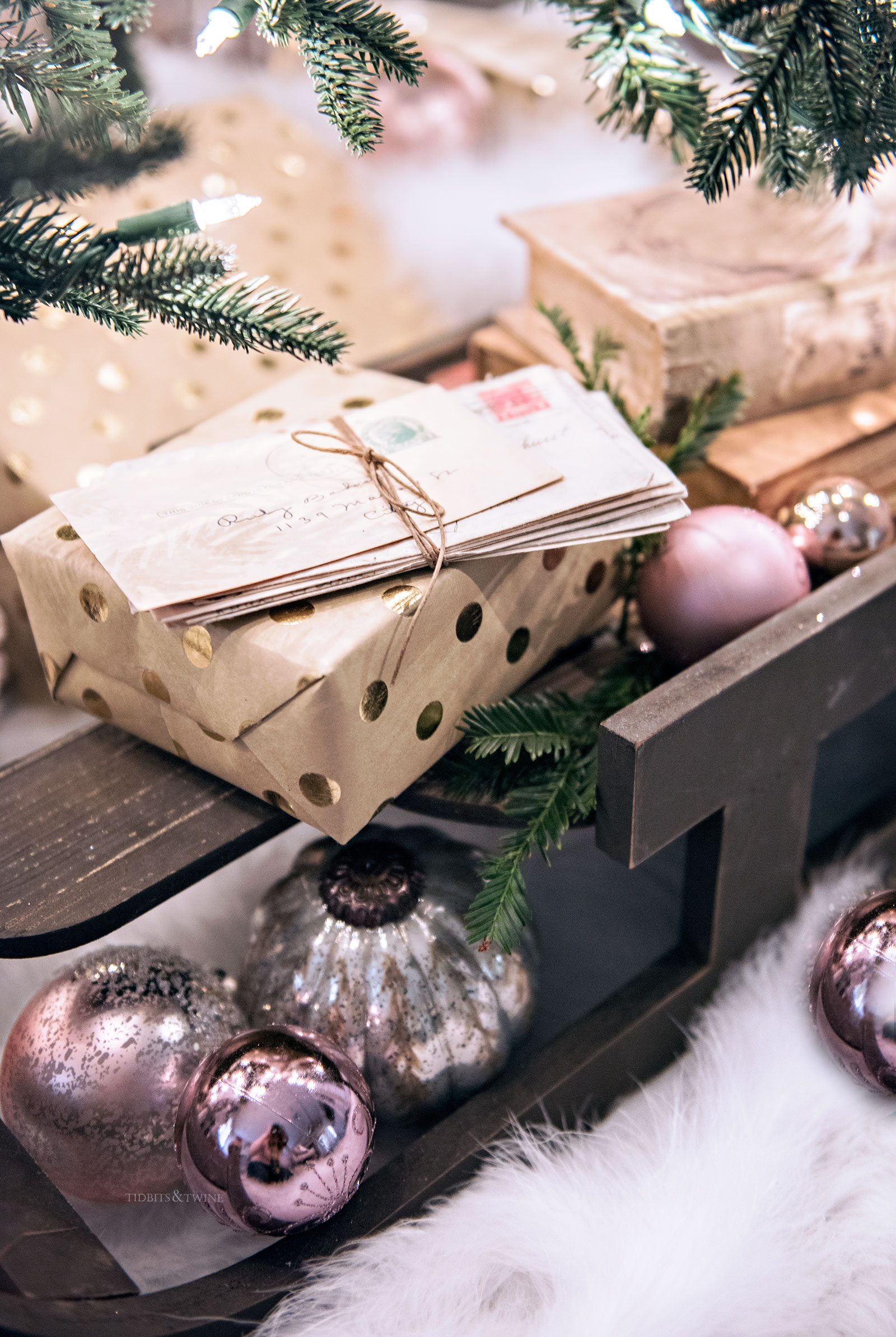 sled underneath a christmas tree with old letters and books stacked on top with pink ornaments