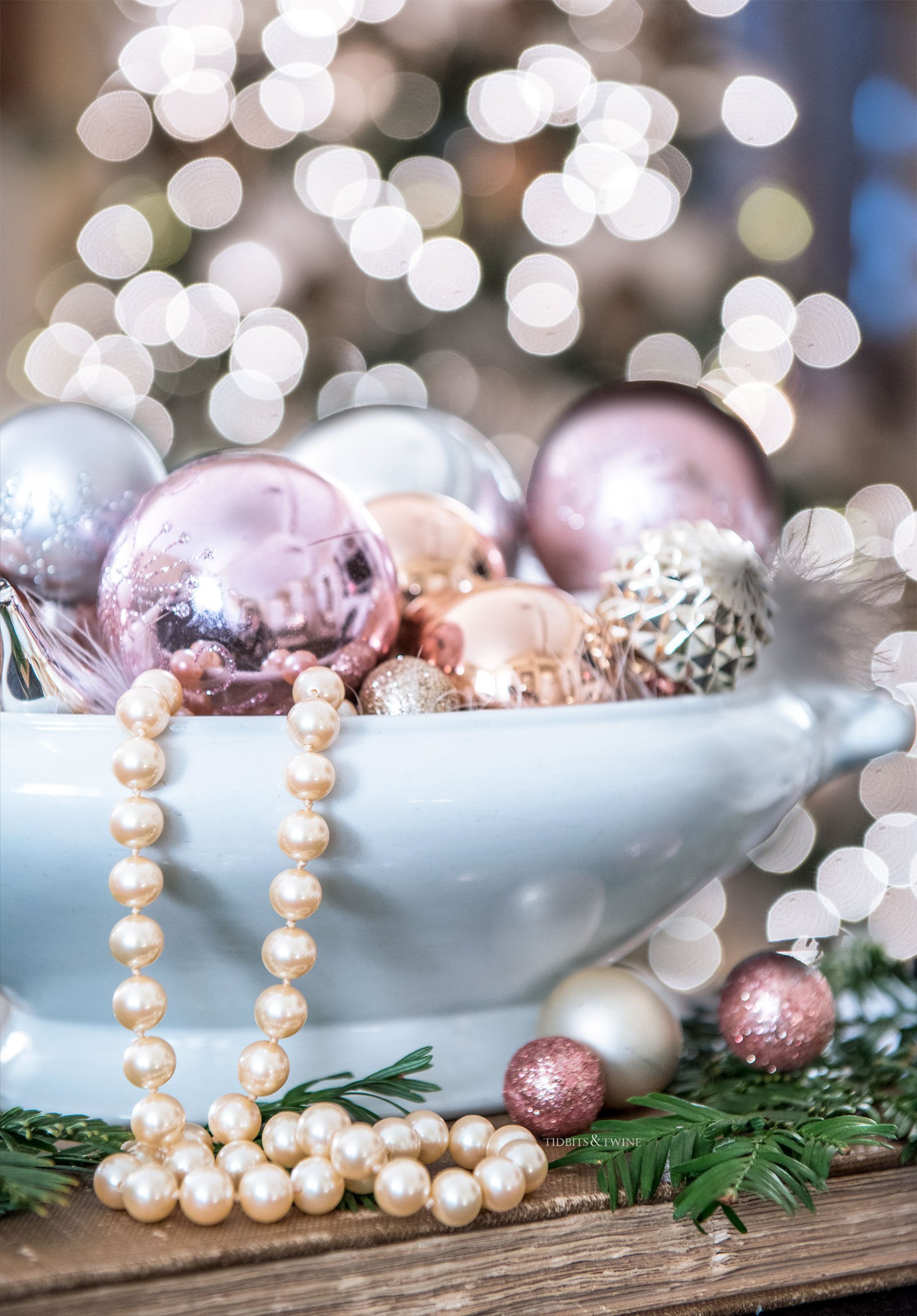 white ironstone bowl filled with pink christmas ornaments and a pearl necklace draped over the edge of the bowl