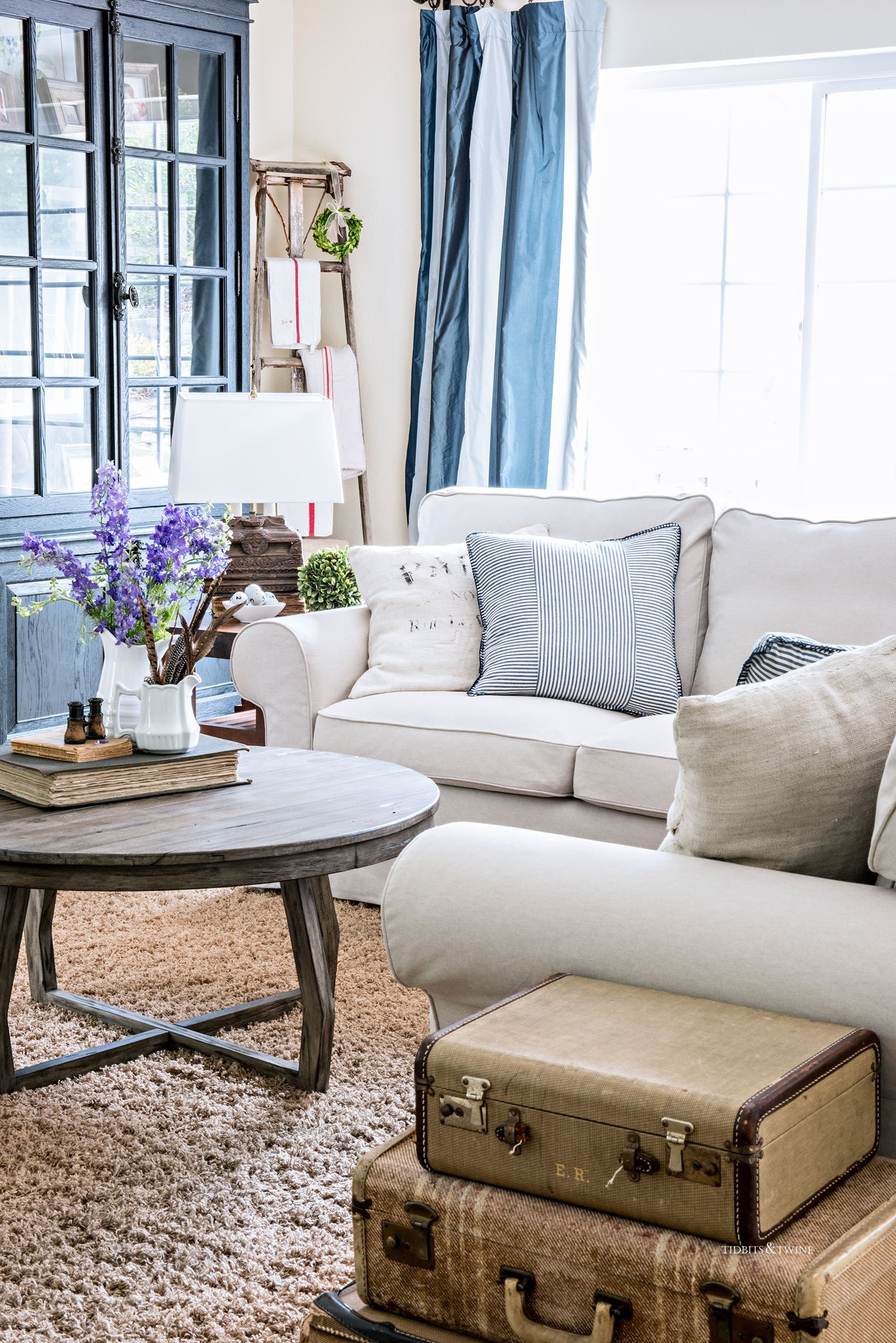 white ikea ektorp section in a living room with round coffee table blue drapes and orchard ladder in corner