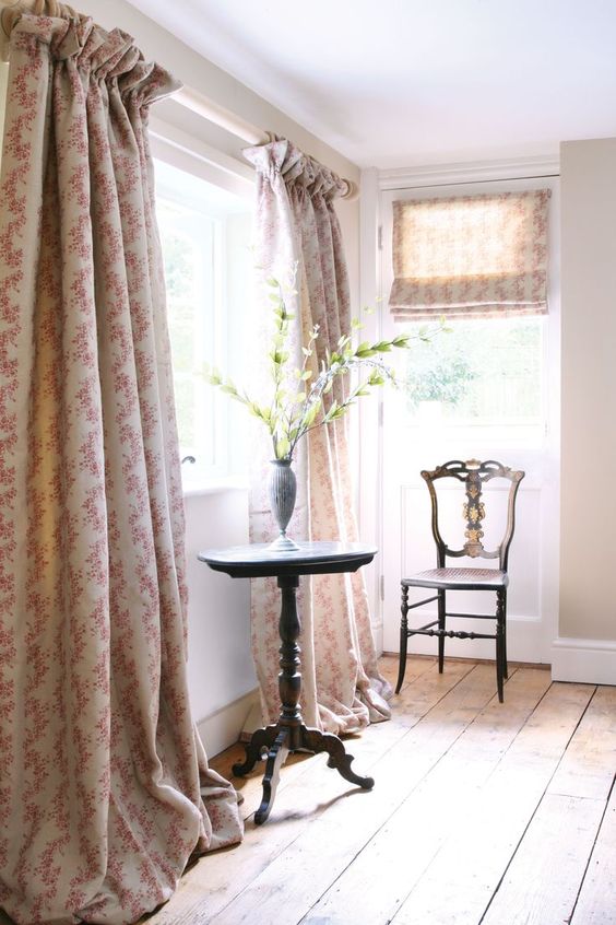 Floral curtains that puddle on the floor with a single chair and side table