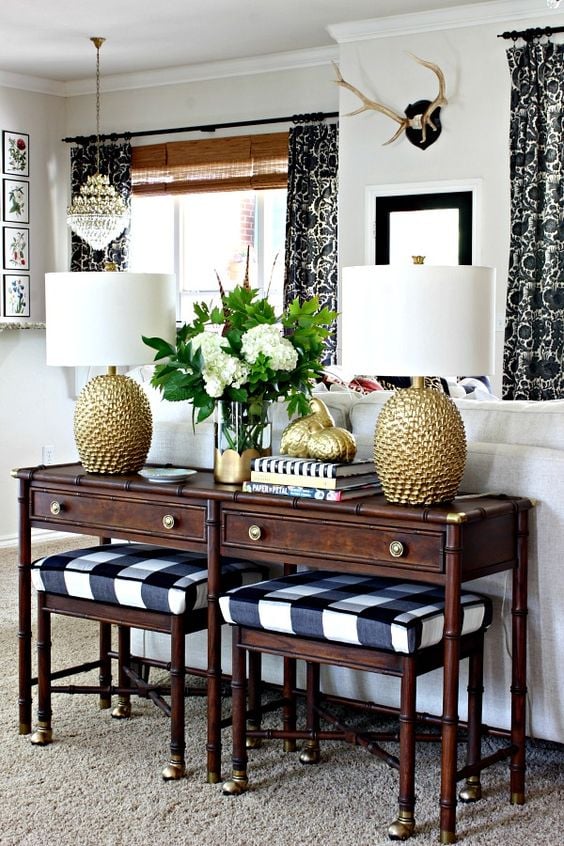 Dark wood sofa table with gold lamps on top and plaid stools tucked underneath