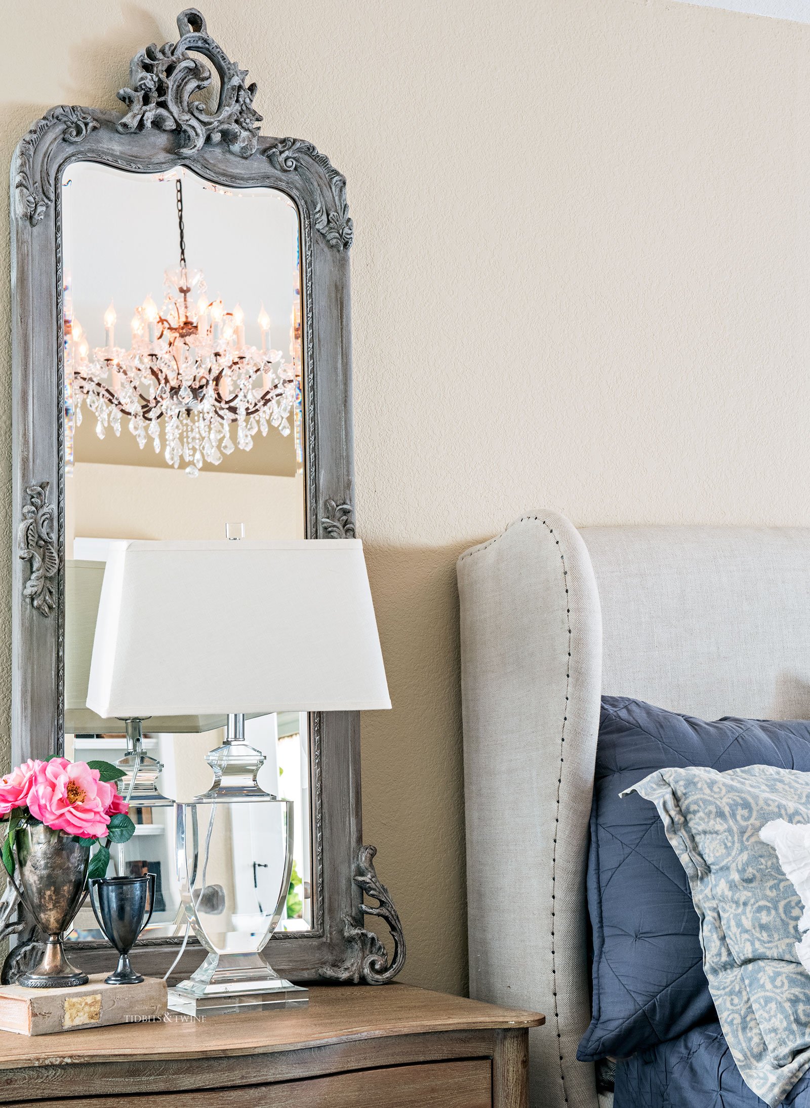 A French master bedroom nightstand with gray mirror and a crystal lamp on bedside table next to linen wingback bed