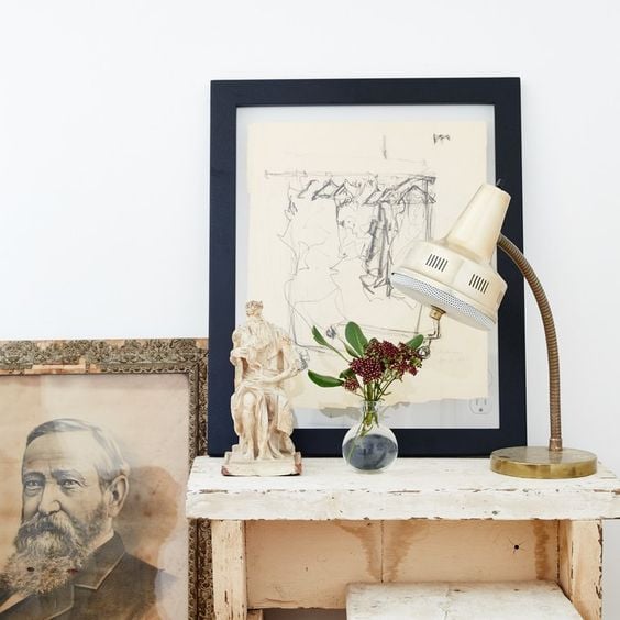 small table with framed sketch leaning on top and portrait leaning on floor next to it