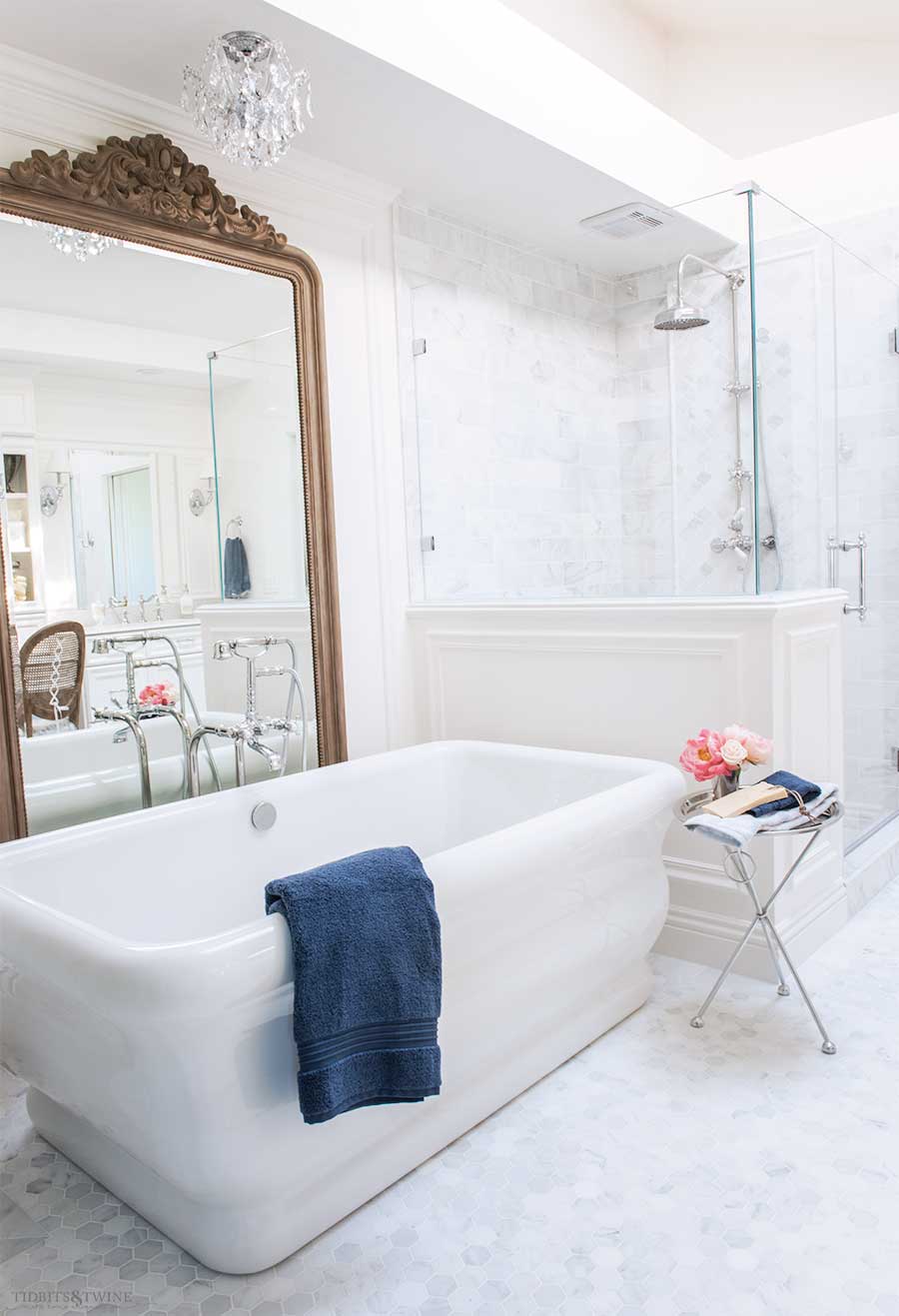 Elegant marble bathroom with freestanding tub and ornate french wood floor mirror behind the tub next to a shower pony wall