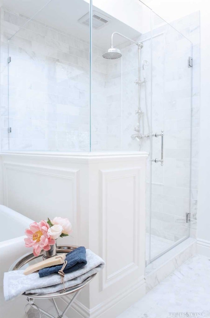 French master bathroom with subway carrara marble shower next to pony wall and freestanding tub with silver tray table