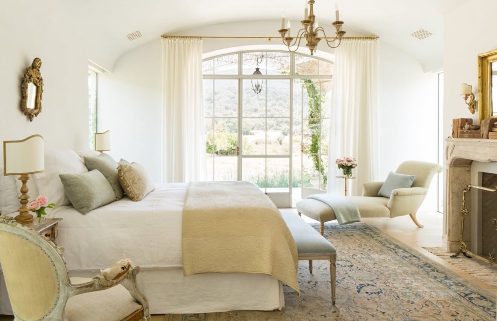 European bedroom with white walls and gold accents and stone fireplace mantel