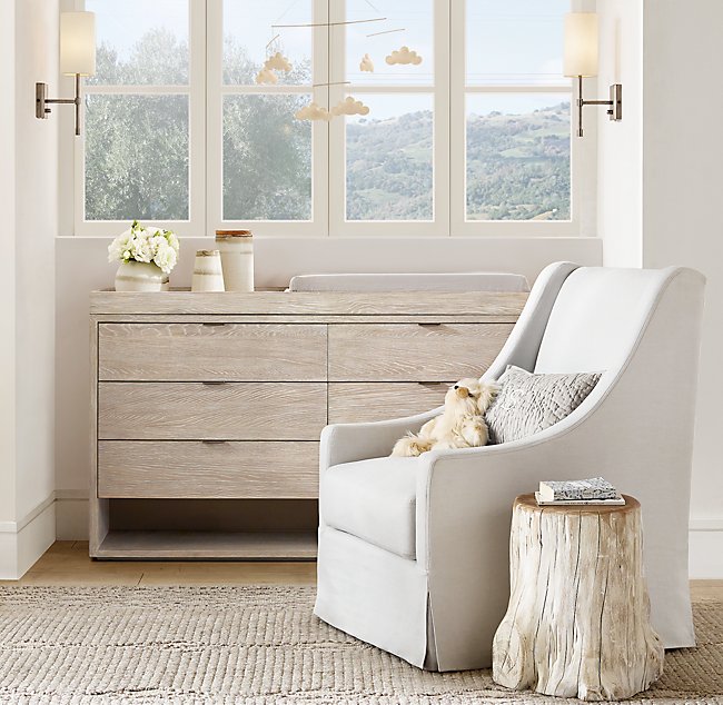 A weathered tree stump used as a side table next to a slipcovered chair in a bedroom