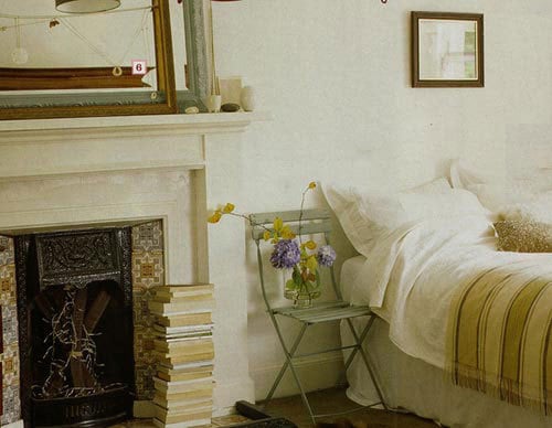 Vintage folding chair as a nightstand next to a bed and a fireplace with a stack of books