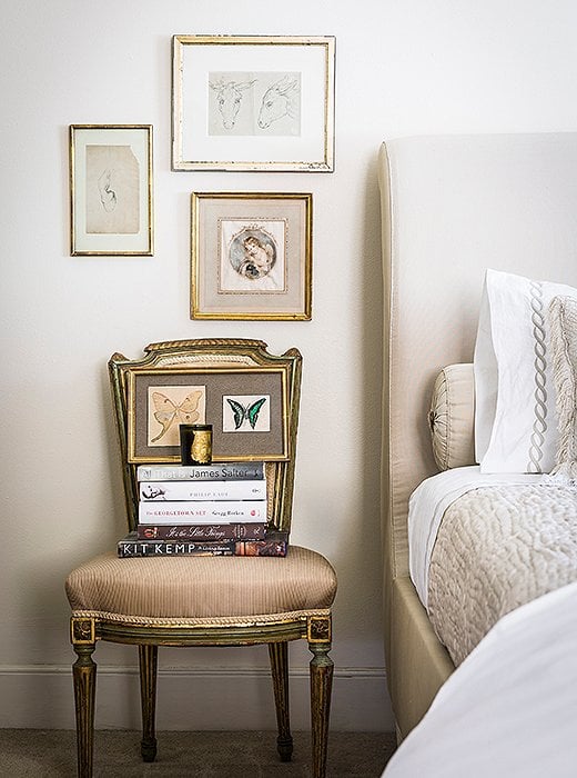 Antique French used as a nightstand stacked with books and art next to upholstered bed