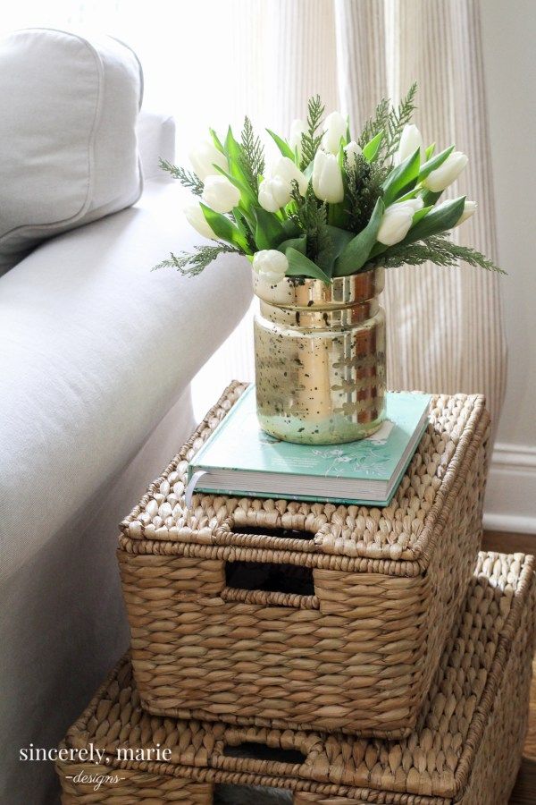 Lidded seagrass baskets stacked as a side table next to a white sofa with a vase of tulips