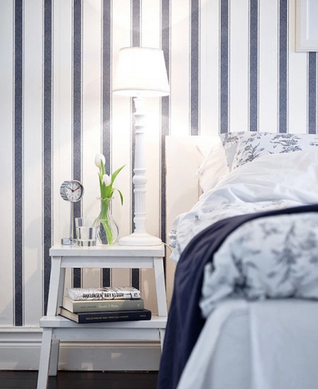 White step stool used as a nightstand next to a blue and white bed with stripe wallpaper