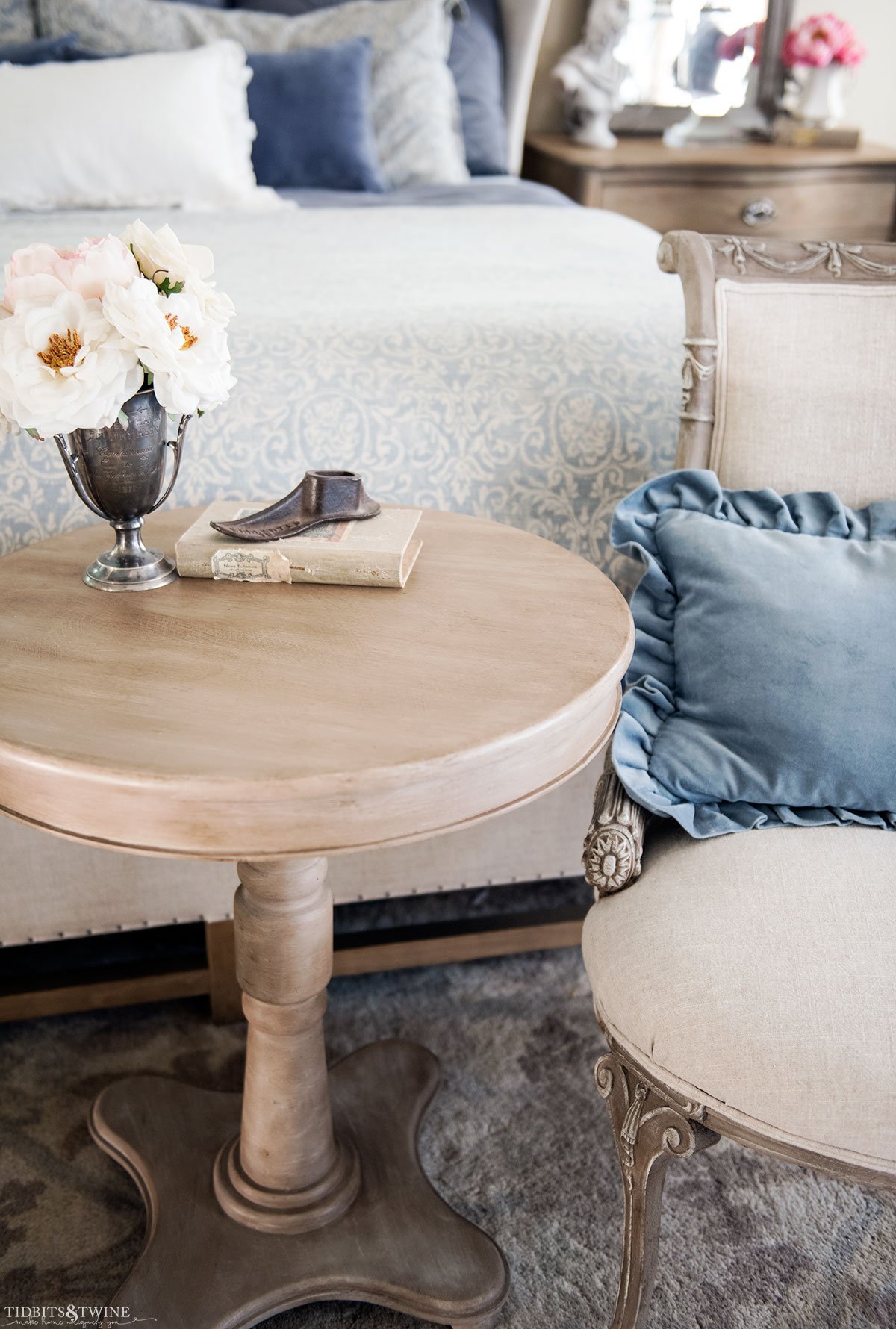 DIY faux wood table and french chairs at end of bed with blue ruffle pillow