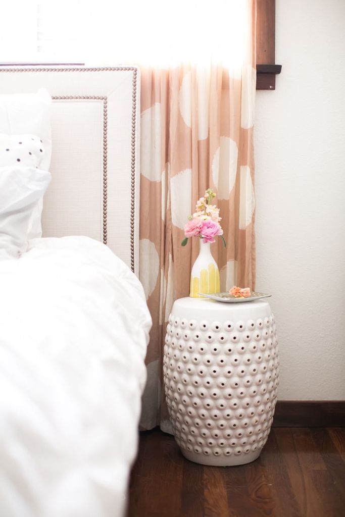 White garden stool as a side table next to a bed with white comforter