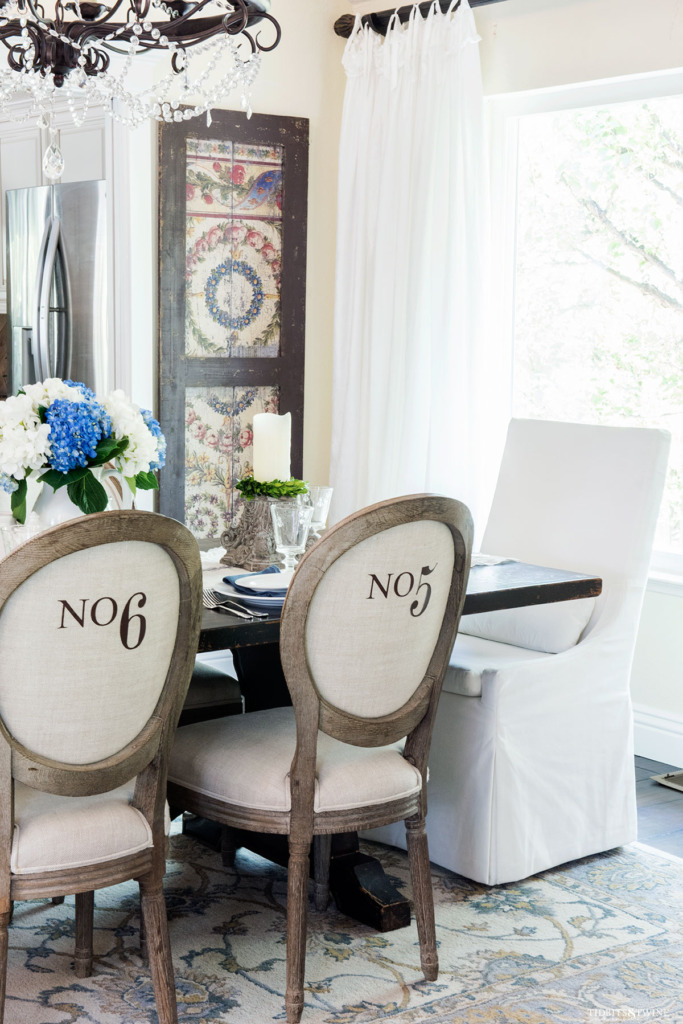 Dining room with round french chairs with numbers on backs and white slipcovered head chair