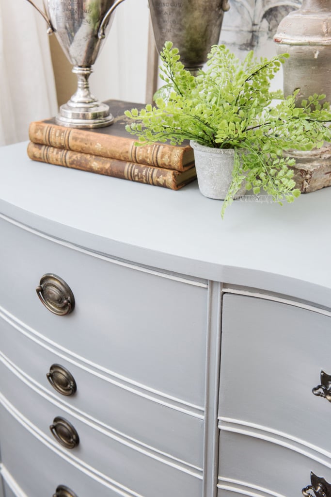 Closeup of antique dresser with gray blue chalk paint with books and trophies on top