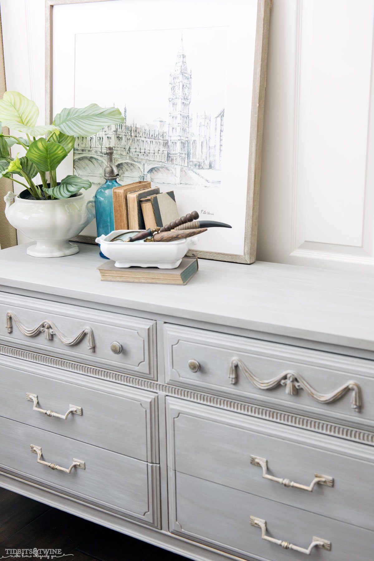 French Linen chalk painted six drawer dresser with swag onlay antique books and seltzer bottle on top with fake houseplant