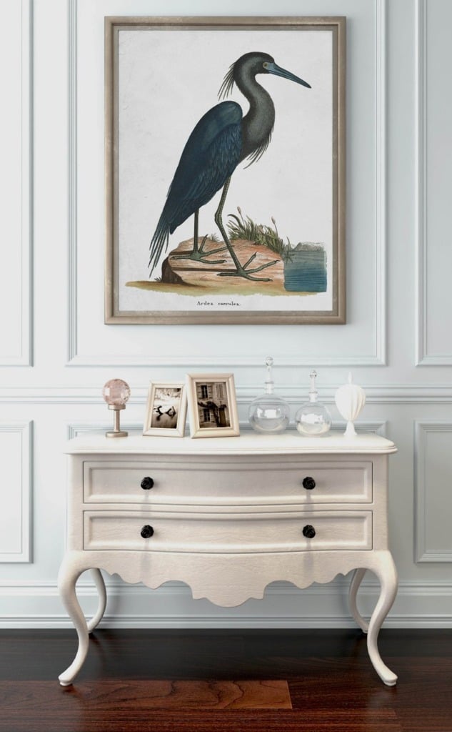 Large artwork image of blue heron hanging above a small chest of drawers