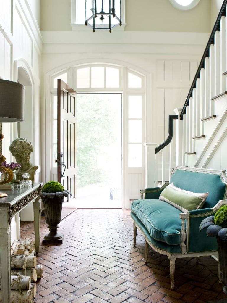 two story entryway with herringbone brick floor and blue velvet settee