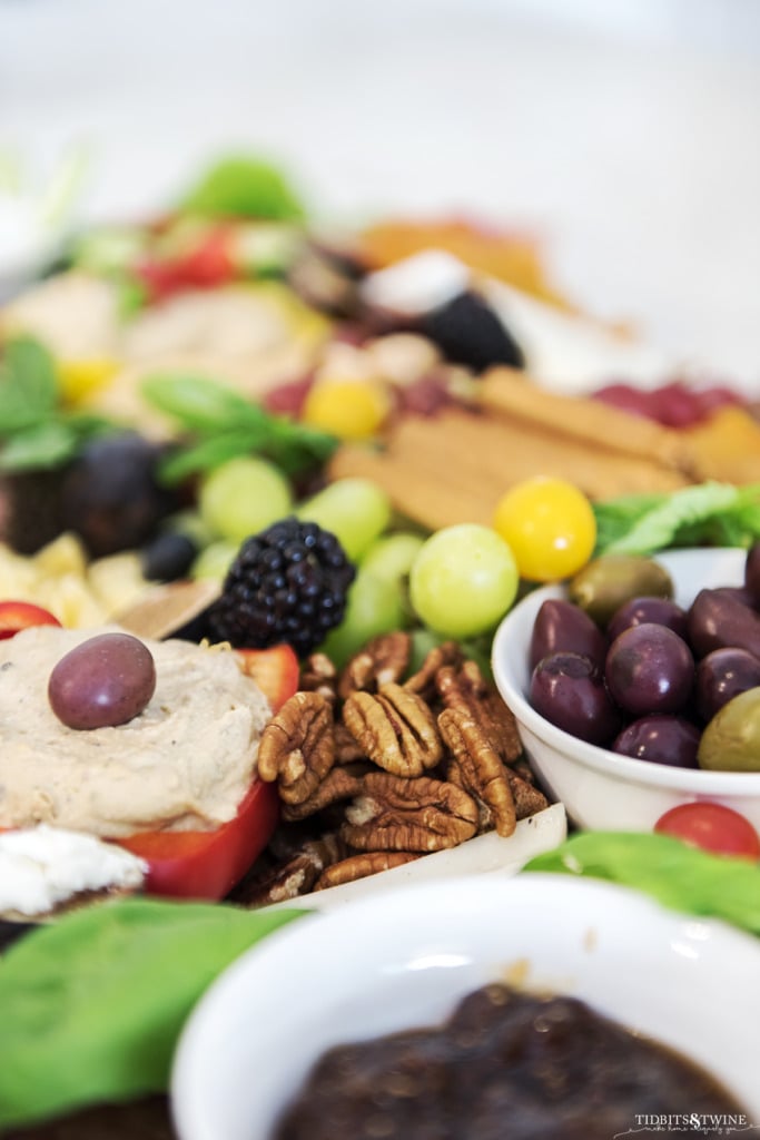 Best charcuterie board closeup of pecans next to bowl of olives and pepper cut in half holding hummus