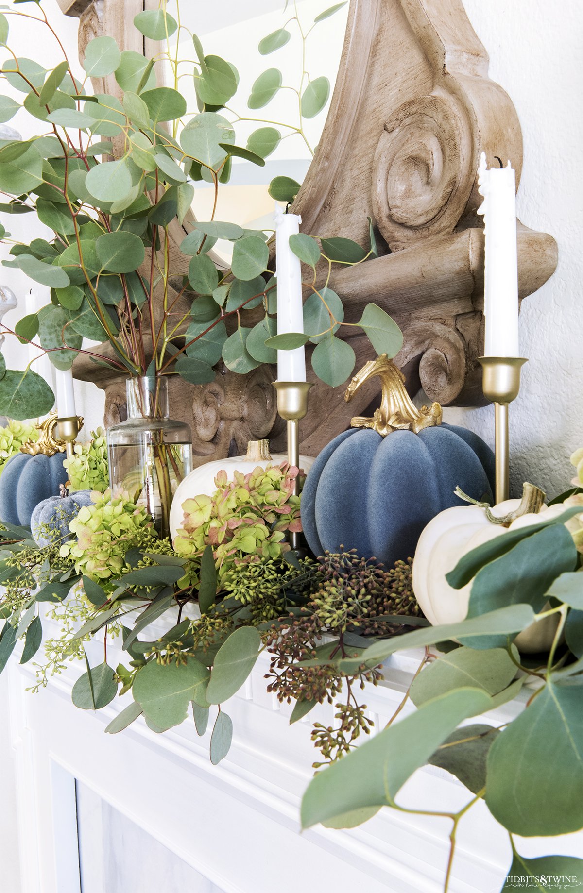 Closeup of blue velvet pumpkin gold candlesticks and eucalyptus on mantel