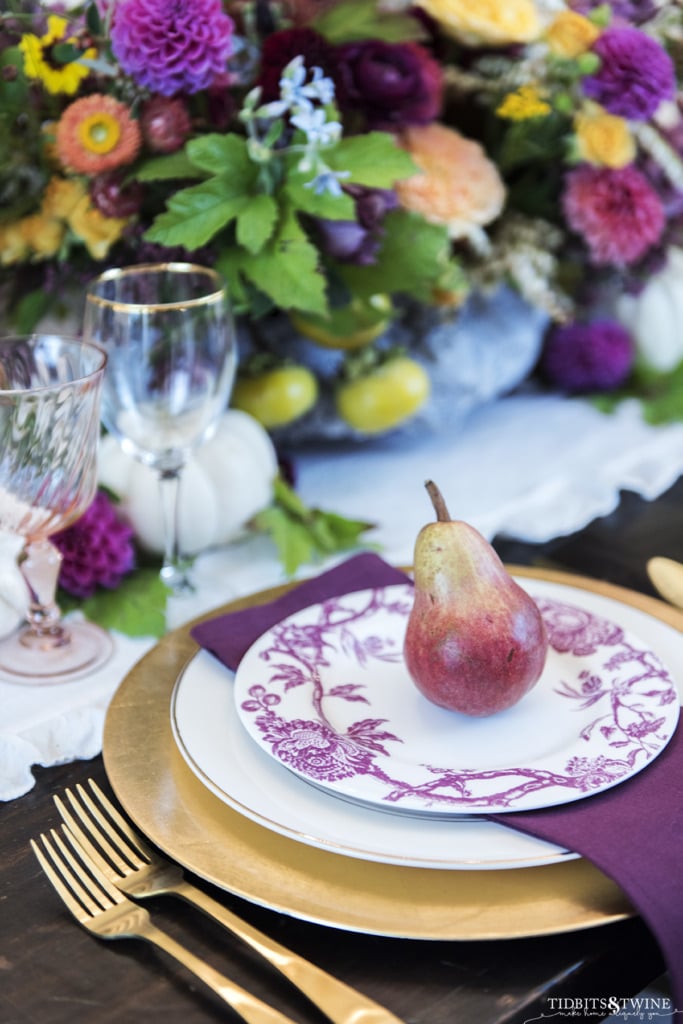 close up of fall table setting in burgandy with red pear on the plate and purple floral centerpiece