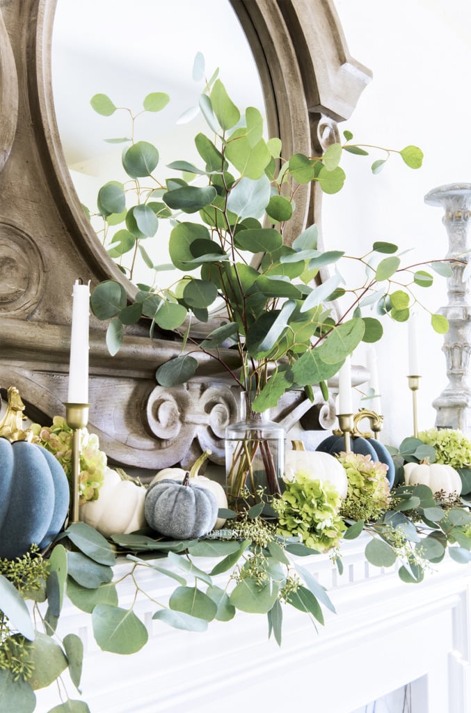 Eucalyptus branches in a vase with little pumpkins and candlesticks on a Fall french mantel