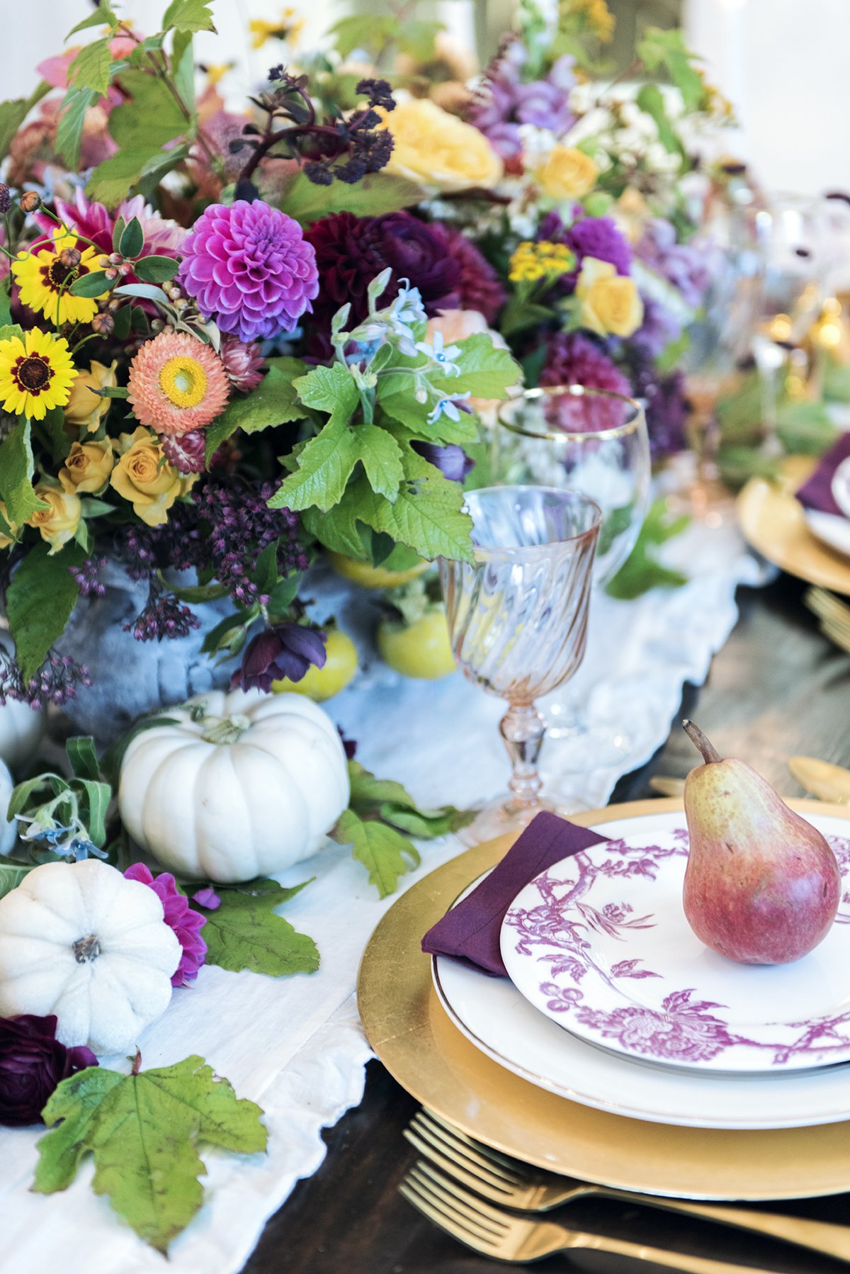 gold and purple fall french place setting with large flower centerpiece and pear on top of plate