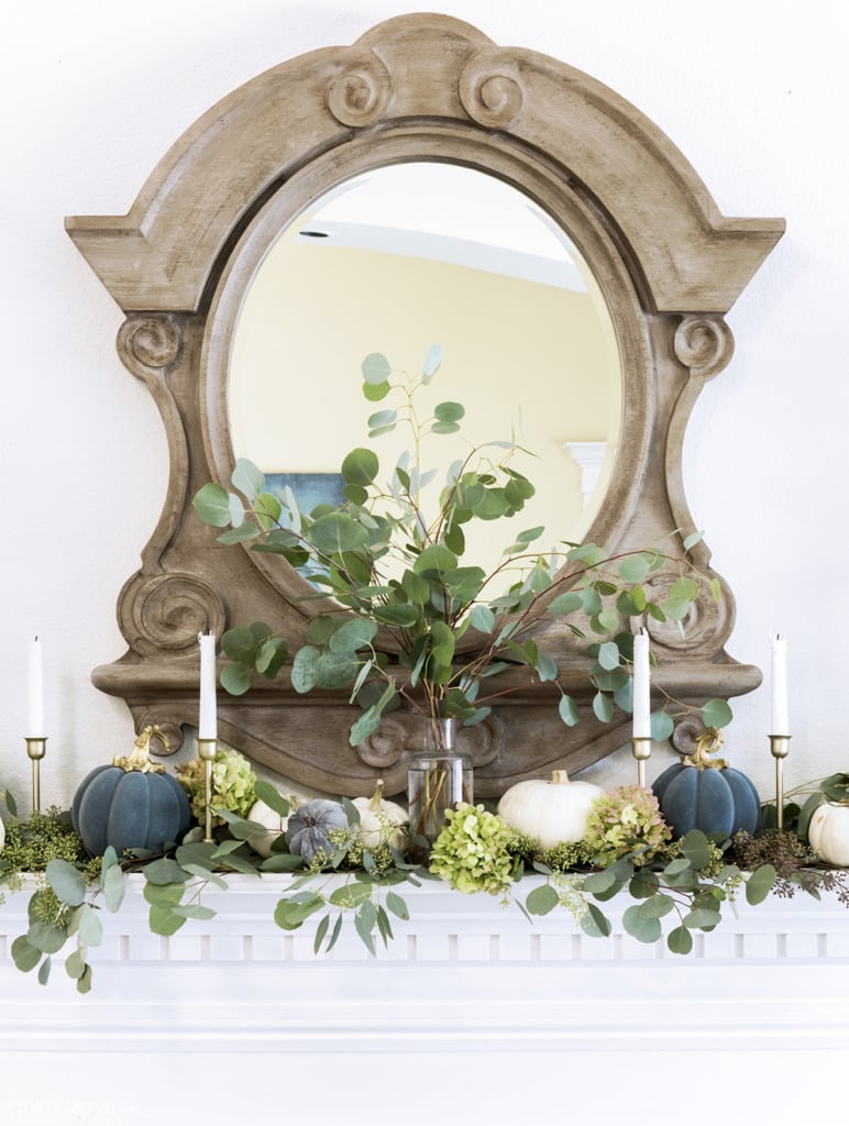 Clear vase on mantel holding eucalyptus with french mirror above