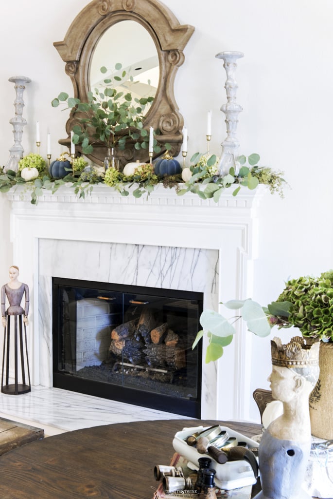 White fireplace surround with candlesticks on top French mirror eucalyptus and pumpkins