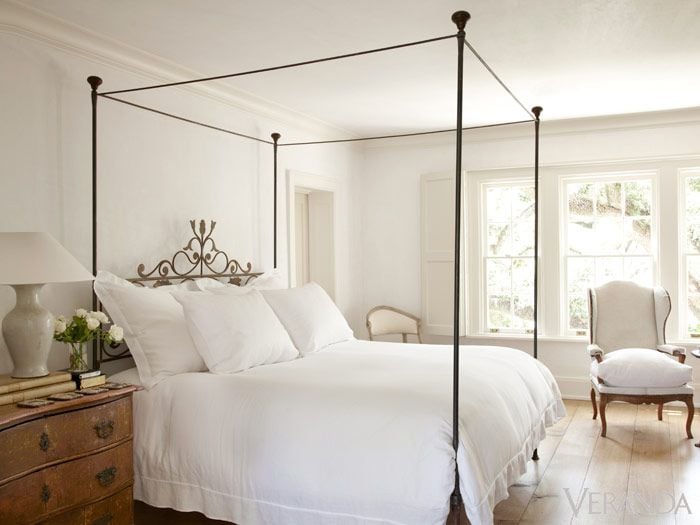 White master bedroom with french iron four poster bed and white linens