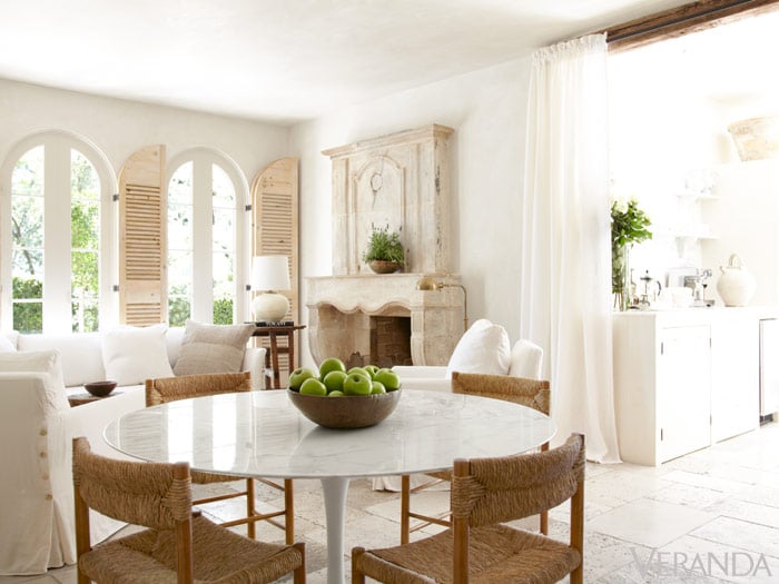 French eating area with round table and rattan chairs on travertine floor and fireplace