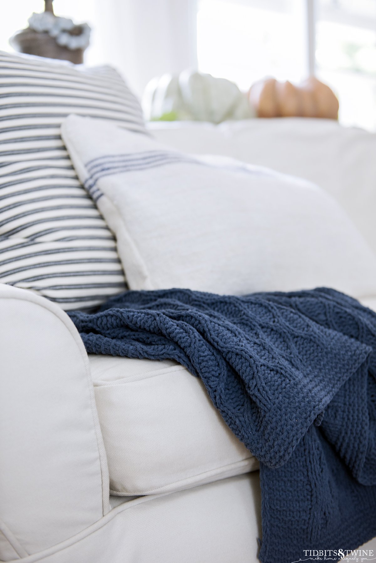 white slipcovered sofa with blue chunky cableknit throw and blue and white decorative pillows and pumpkins in the background