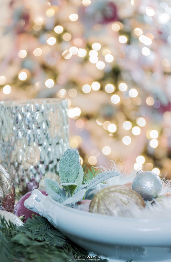 Closeup of ironstone tureen filled with pink Christmas ornaments and tree in background