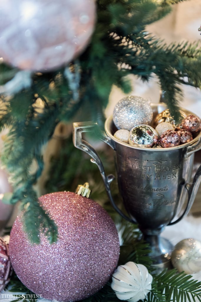 Vintage trophy cup filled with pink and gold ornaments underneath a Christmas tree