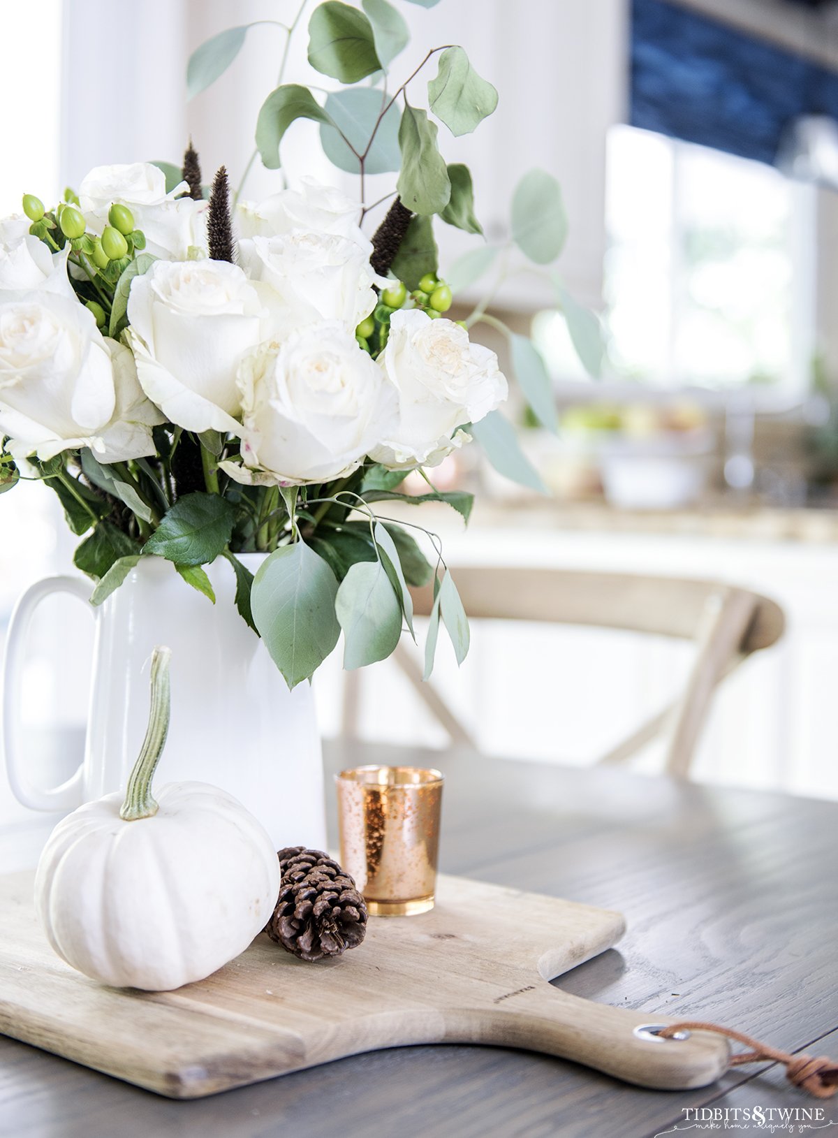 Fall kitchen table centerpiece with white pitcher holding roses and eucalyptus and small white pumpkin at base