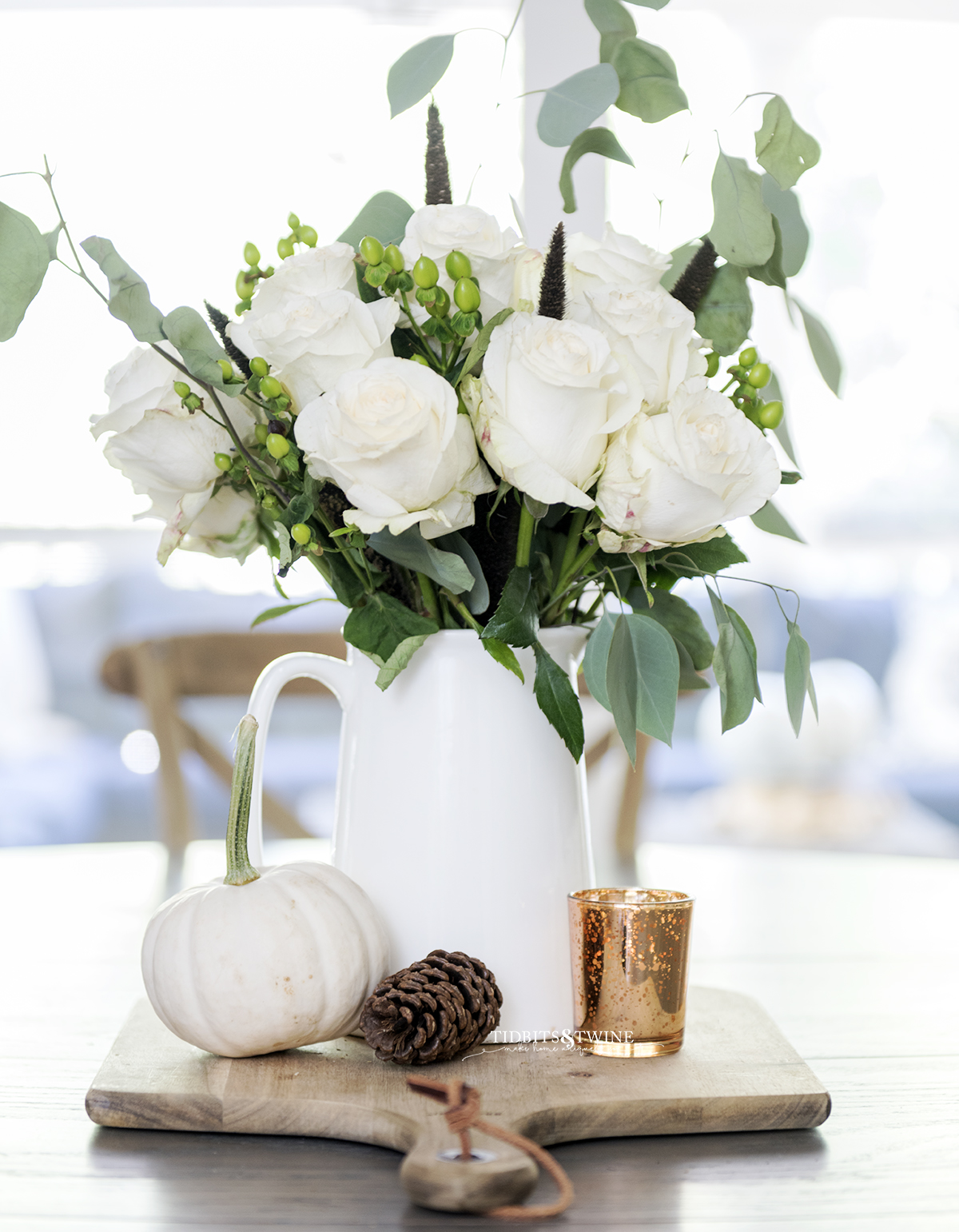 Fall kitchen table centerpiece with white pitcher holding roses and eucalyptus and small white pumpkin at base