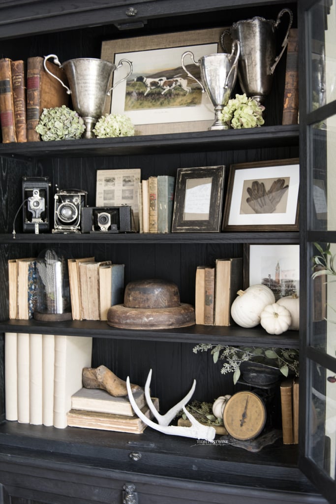 black french cabinet decorated for fall with antique books trophies and dried hydrangea