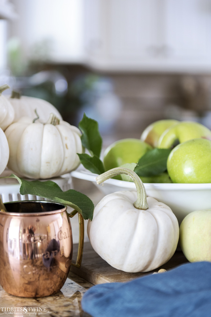 Fall vignette with white pumpkins and green apples with a copper mule mug