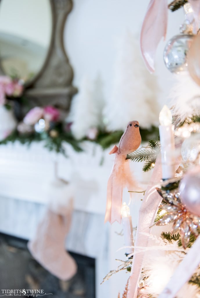 Pink bird and candle clip on Christmas tree with French fireplace mantel in the background