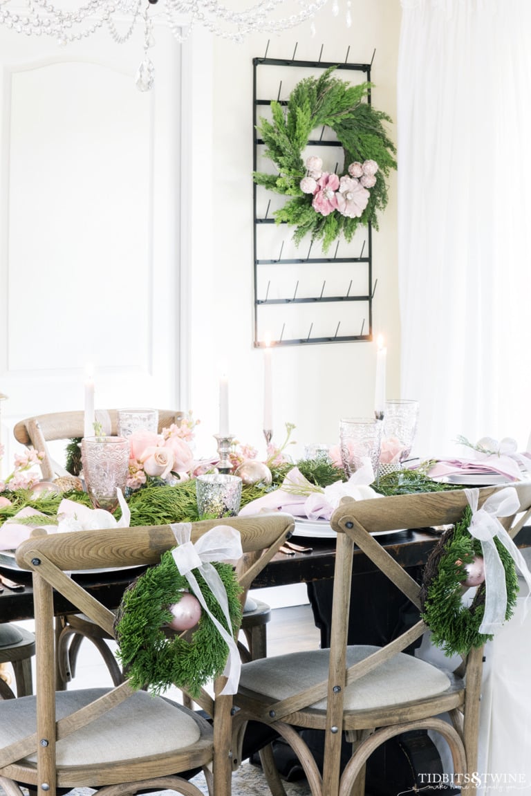 dining table with crossback chairs with pink white and green tablescape and small wreaths on backs of chairs