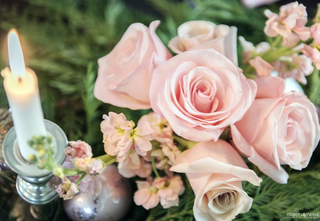 Closeup of pink roses and white candles surrounded by cedar garland on Christmas table