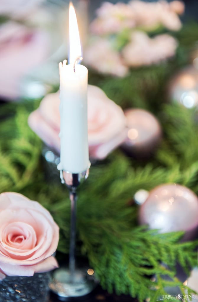 Closeup of taper candle with dripping wax and Christmas pink and green table in background